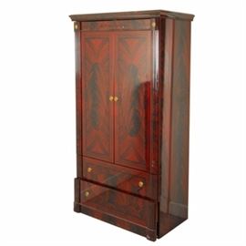 Neoclassical Style Flame Mahogany Wardrobe: A Neoclassical style wardrobe in flame mahogany veneers, having a gloss lacquer finish. The flat top has a simple molded cornice, above a stenciled frieze and two doors with oval and book-matched panel, above two drawers with horizontal panels, between reeded stiles with gilt rosettes. The interior is veneered in a light wood and having a hanger bar, belt / tie rack and mirror mounted to inside door.