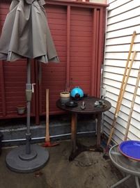 Patio umbrella & stand, small wooden patio table, a few yard tools, one of a pair of small glass-top patio tables