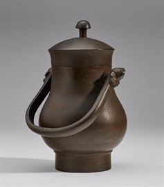 Antique Chinese Bronze Ritual Handled Wine Vessel    Antique Qing dynasty Chinese bronze ritual handled wine vessel. The lidded bronze vessel has a swing handle terminating in a mask decoration. The pear form body has subtle allover engraved decoration inlaid with paint. Chinese ritual bronzes were used in offerings of food and drink to ancestors in family temples, ceremonial halls or at ritual banquets in which living and deceased members participated. They were eventually buried with the owner so they could continue to pay their respects in the afterlife. Good condition. Measures 8.7 inches high x 4.7 inches wide.