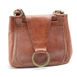 Vintage Handcrafted Leather Handbag: A vintage handcrafted brown leather handbag. This sturdy leather bag features dual handles with brass ring anchors, a tapered front flap with a large brass O ring accent and an unlined interior. A large C is embossed to an interior pocket.