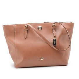 2016 Coach Leather Turnlock Tote: A 2016 Coach Turnlock tote in light brown crossgrain leather. This generous satchel has adjustable buckled double handles and silver tone hardware. The handbag has an outside slide pocket with a turnlock closure, an interior zippered pocket and utility divider pockets, being fully lined in Coach print fabric. The bag bears a leather creed patch as well as a label reading, “No. C1680 37142.”