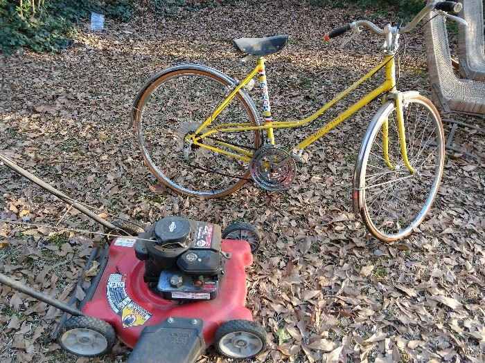 Super Duper vintage 10-speed women's bike "Belle De Paris", in Mellow Yellow, part of their Tour de France collection, by Astra. Astride this man-magnet bike is a lovely Briggs & Stratton 300 series side discharge push mower. It's soon to be Speedo season, so get those glutes in shape by pushing this baby around your white picket fence!