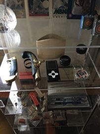 Display case of small items. Lighter gun. Mp3 player. Cubs pins. Vintage Swingline staplers
