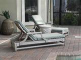 TWO OF MANY TEAK CHAISES AND STONE TABLES