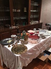 Collectible brass and pewter serving platters, glass vases, porcelain cakes stands etc.  Notice all of the glassware on the shelves in the back.