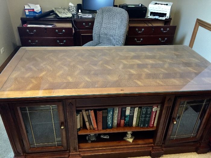 BUY IT NOW!  Lot #101 - Beautiful Executive Desk.  Two cabinets in front with leaded glass doors & glass shelves.  Desk has a thick glass top to protect the herringbone pattern design.  It has seven felt-lined drawers.  $750
