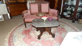 MODIFIED WALNUT BASE MARBLE TOP VICTORIAN TABLE. EAST LAKE WALNUT FRAME UPHOLSTERED SETTEE, RUFFLED CRANBERRY CASED GLASS WEDDING BASKET. CHINESE CIRCULAR FRINGED EDGE WOOL RUG.