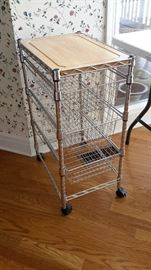 Chrome serving cart with Cutting board top and three drawers.