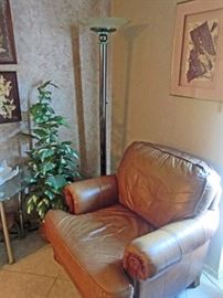 Brown leather chair matching sofa, tall floor lamp, artificial plant 