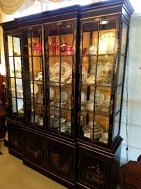Chinoiserie decorated lighted display cabinet displaying several sets of china and some decorated ruby glass on the top shelf.