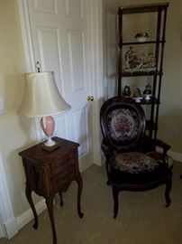 Carved stand with two drawers, Needlepoint upholstered arm chair, Etagere in the corner displaying porcelain and ceramic items