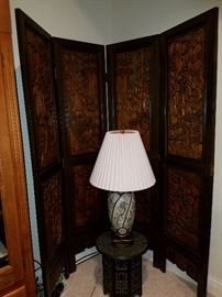 Carved 4 panel screen behind a carved stand and oriental style lamp