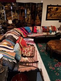 Long curved sectional sofa, leather.  Displays collection of southwest rugs (some American, some Mexican).  Navajo examples have 'issues' and losses