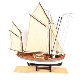 A large handmade model wooden sailboat. The hull of the boat is painted blue, white, and black. The boat is on a black stand, and sits atop a custom made wooden board stand. Dimensions: 40.0" W x 40.0" H x 12.0" D - board: 25.25″ × 5″ × 0.75″ - boat: 32″ × 33″ × 8″ 