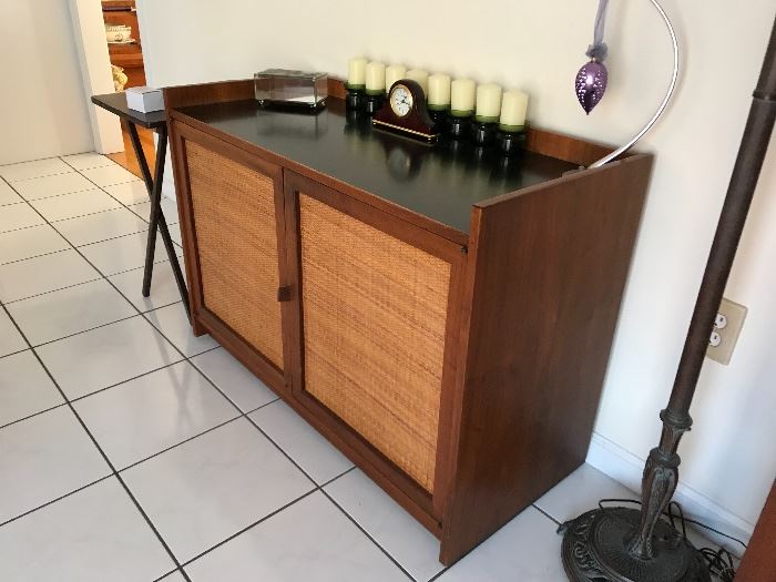 Beautiful mid century modern walnut and caned door rolling bar server credenza by Founders. This bar is in excellent condition with very light signs of use over the years. Solid walnut construction with a smooth black laminate top perfect for mixing drinks without staining the wood. Nice woven cane door design with leather pull. Drawer and doors open smooth and freely and has great space inside.

Measures 42 wide x 18 1/4 deep x 29 1/4 tall