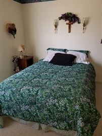 Queen bed with bedding, wood nightstand and wall decor.