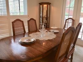 Vintage oval dining table with 3 leaves and 6 chairs. Lighted curio cabinet in far corner.
