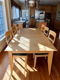 Long, blonde kitchen table with 8 chairs. Chairs upholstered in leather.