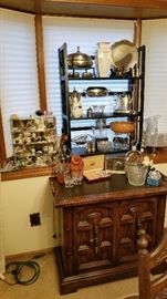 Overview of silver plate, vintage glass, Lenox vase, soapstone bear, Carved Jade dragon, Michael Aram frame, set of Carvel Hall Knives on vintage cabinet