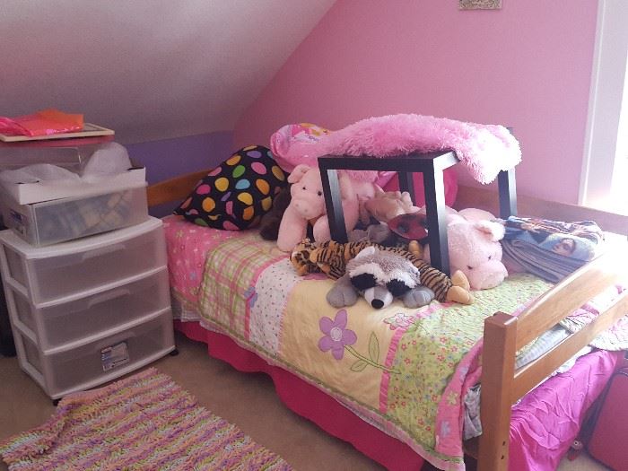 Twin bed with girl's bedding and stuffed animals, small end table and plastic storage bins