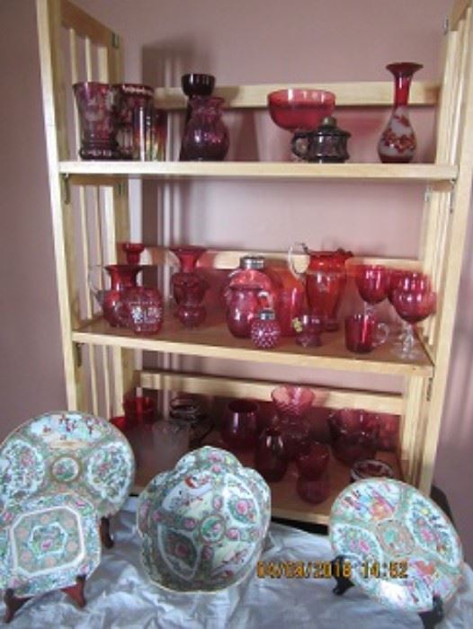 Cranberry glass on the shelves is a part of all that is in the sale.  The purple glass oil lamp on the top shelf is unique. The Chinese export dishes and bowl on the table is all in good condition. Ruby stain is also seen.