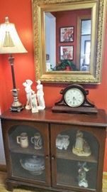 mahogany cabinet with glass doors, gold ornate mirror, lamp, and Greek statues 