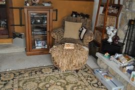 Glass-front cabinet with fishing collectibles, ducks and decoys, leather fringed rug, over stuffed chair with matching ottoman, tall hall tree with baskets and hooks, candles galore, area rug