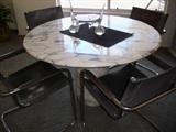 Round marble dining table with 4 gray leather and chrome chairs.