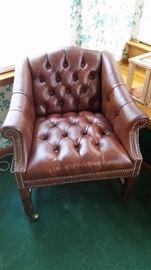 2  tufted leather chairs with rolled arms with nail head trim accents and metal casters.