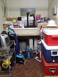 The utility room is overflowing with coolers, vacuum cleaners, heaters, & more 