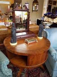 Drum table with lower book shelf, leather top.  Displaying a pair of black basalt figures, a small music box, and a shaving mirror