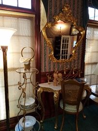 Gilt metal stand with glass shelves beside a gilt console table (marble top) and ornate gilt mirror