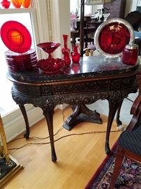 Curved front carved table with black marble top displaying red glass