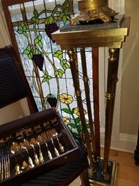 The other stand.  On chair: Gold tone flatware.  Behind chair, a grape and floral design stained glass window