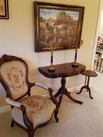 Needlepoint upholstered arm chair next to a flip-top game table and a small leather top stand.  