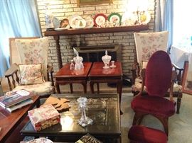 overview of very full living room, pair of tables with cocktail slide outs, coffee table carved top with glass, small rocker with foot stool, pair of slip covered side chairs. 