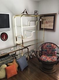Modern brass and glass etagere, one of a pair of bamboo swivel chairs, framed hooked rug picture