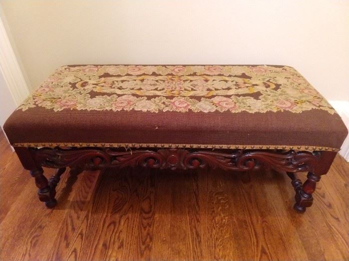 Renaissance Revival upholstered bench, late 19th cent., of rectangular form, the seat upholstered in floral needlepoint on a chocolate ground, with brass nailhead trim, above block and turned legs joined by a pierced carved scrollwork front stretcher; measures 17"h x 39"l x 18"w.