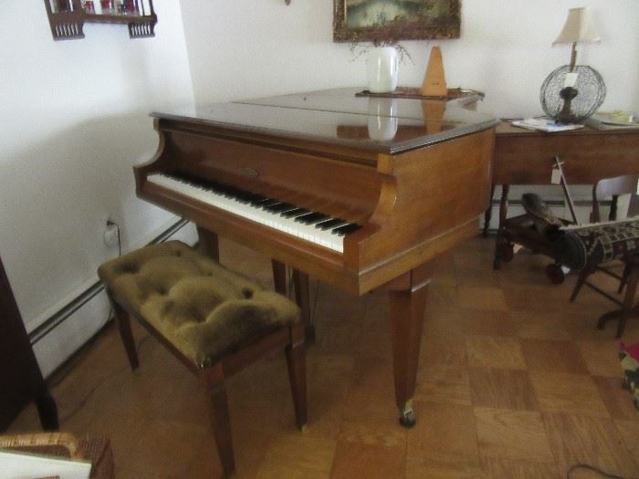 Wurlitzer grand piano with bench. There are many music books, and on the piano is a metronome.  