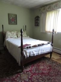 High post double bed. The carpet on the floor is oriental. The art on the walls are needlework.