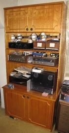 This bookcase is full of vintage audio equipment, with a few VHS tapes, and more.