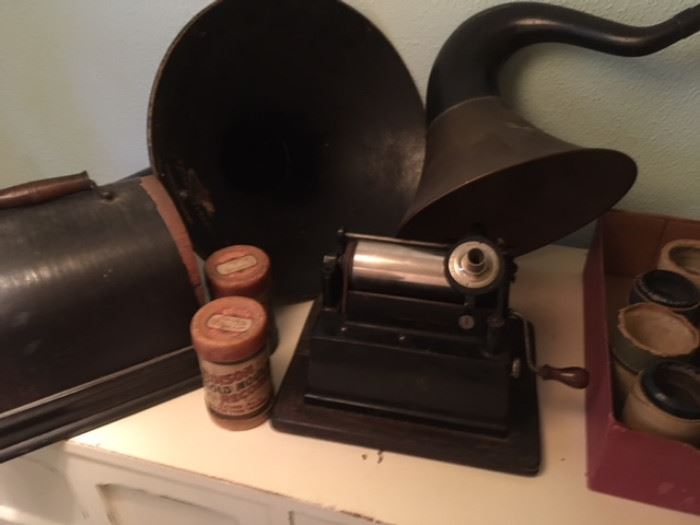 Edison phonograph in travel case, along with numerous cylinder records; in background are victrola horns