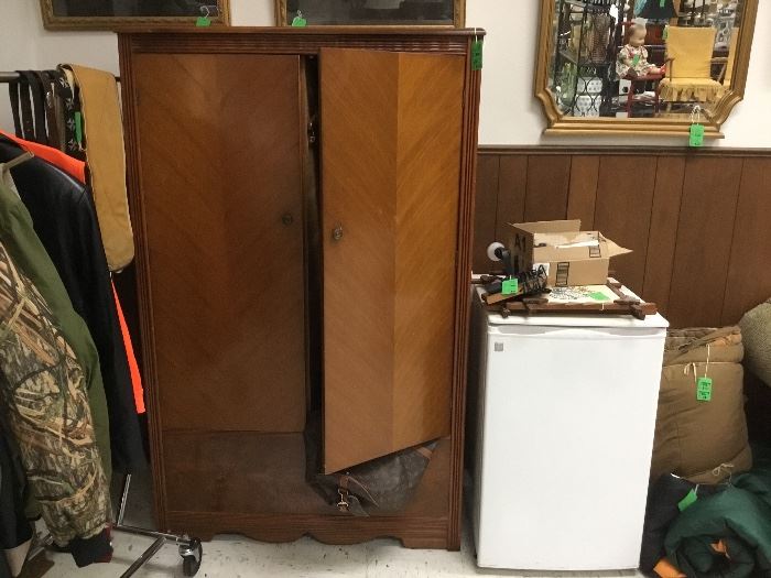 Armoire and small refrigerator, sleeping bags and men’s Gun cases and hunting clothing. Pictures and mirrors along the walls. 