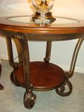 Fortunado Oval cocktail Table with two matching Round End Tables. Distressed Cherry with Glass Top. Swirls of antique bronze cast metal supports glass top. Oval table is 31' x 50". Round end tables are 27".