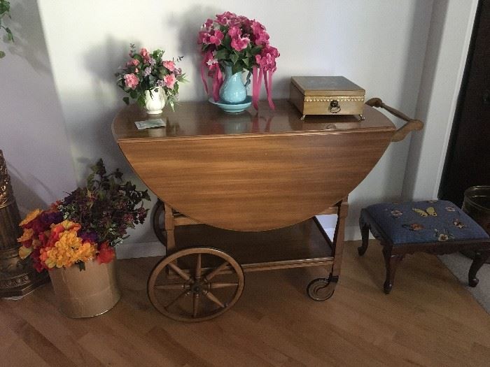 Antique tea cart with small drawer and glass tray.  Cross stitched foot stool, silk flowers. 