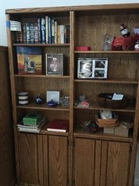 Book case with shelves and cabinet area. Books, candles, small binoculars, crock, Longaberger basket with two liners, Longaberger candle and crock.