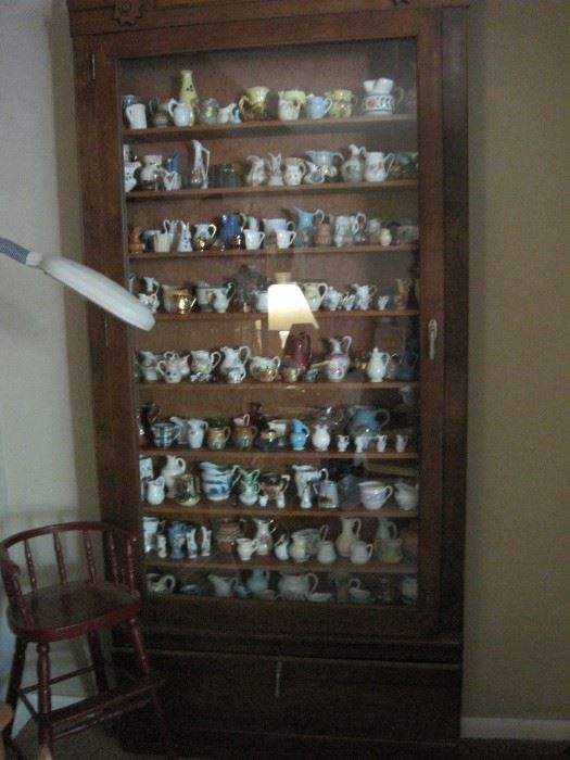 collection of small pitchers in tall narrow cabinet & youth chair