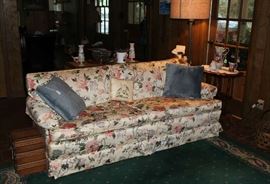 Sofa in den with rose colored flowers.