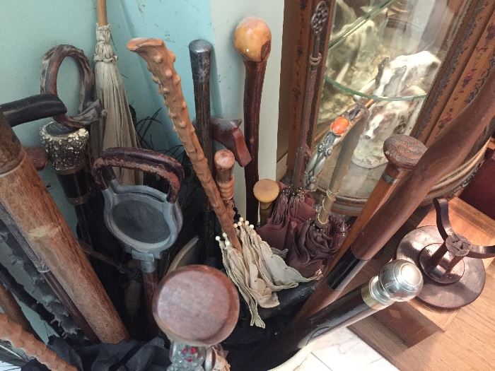 A large group of walking sticks, antique umbrellas, and anti-canes while standing in antique porcelain and pottery containers