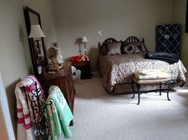 Bedroom with two cross stitch quilts, foot stool with another quilt and more